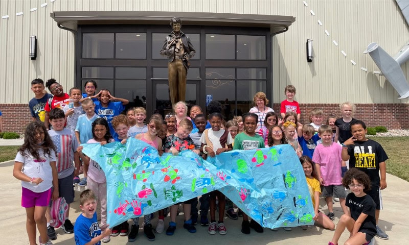 Group of students with banner standing before Amelia Earhart statue