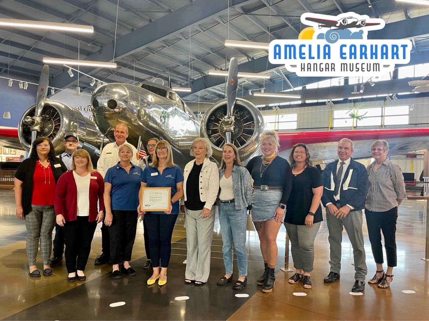 Museum team taking picture with GEMmy award in front of Lockheed Electra